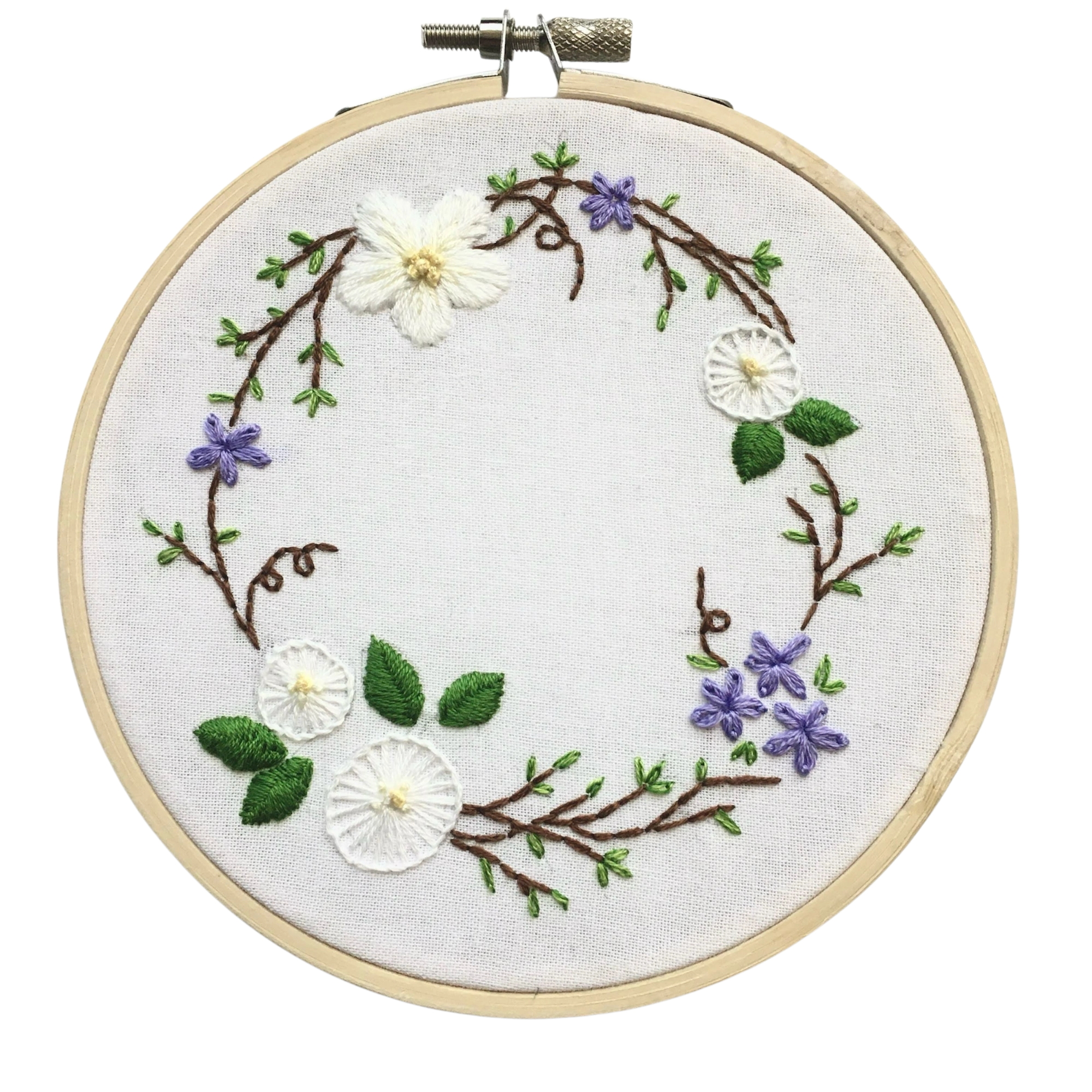 A circular embroidery hoop containing floral embroidery on white fabric. The design features white flowers, purple blossoms, green leaves, and brown vine branches arranged in a wreath-like shape on a plain white background.