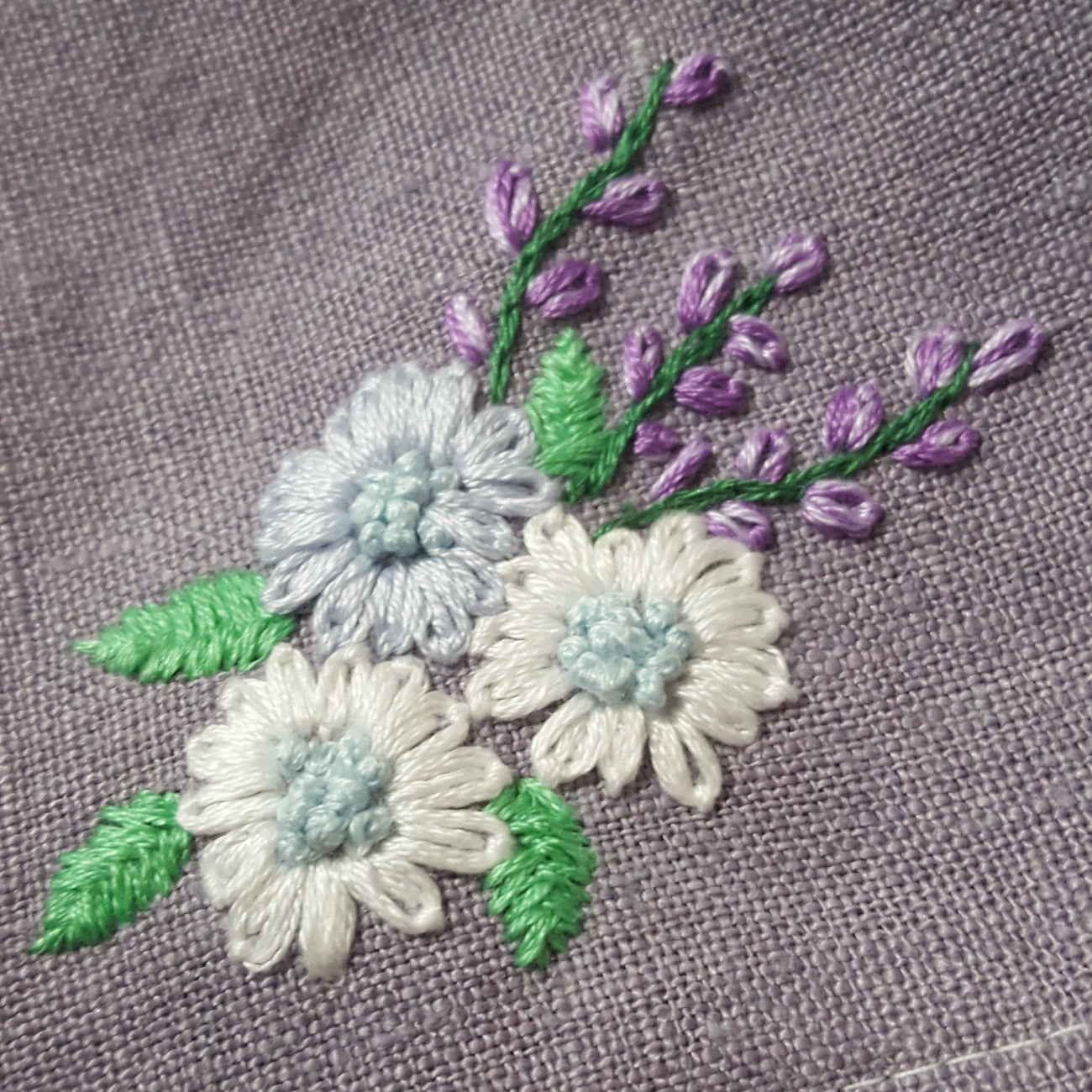 Close-up of embroidered flowers on a textured lavender-gray fabric background.