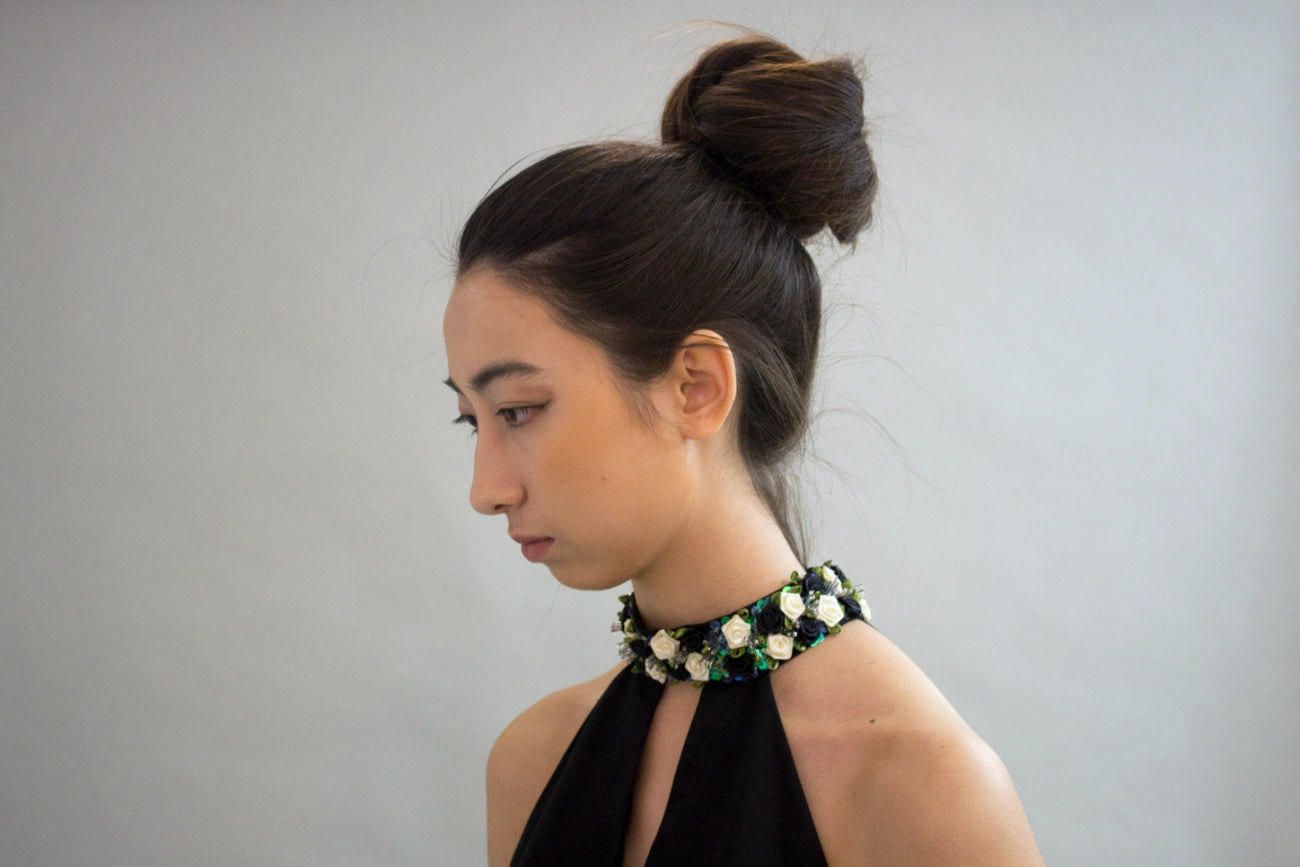 A woman wearing a black halter top and a chunky beaded choker necklace with black, white, and green beads, set against a plain light gray background.