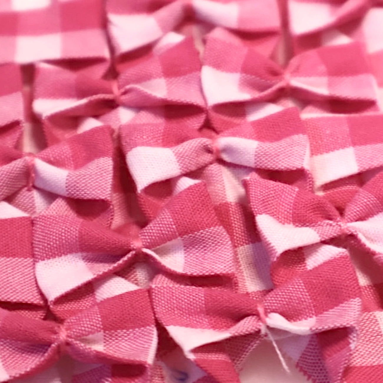 A close-up of multiple small fabric bows in a pink and white gingham check pattern, overlapping each other.